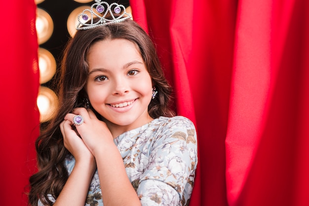 Smiling Cute Girl with Crown in Front of Red Curtain