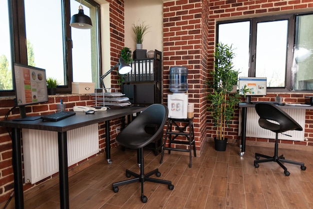 Close up of empty corner with desks in startup office, computer, modern equipment and bookshelf with decor in business space. Workplace with technology and instruments for work