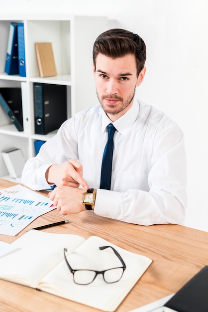 Young businessman pointing finger at watch in workplace