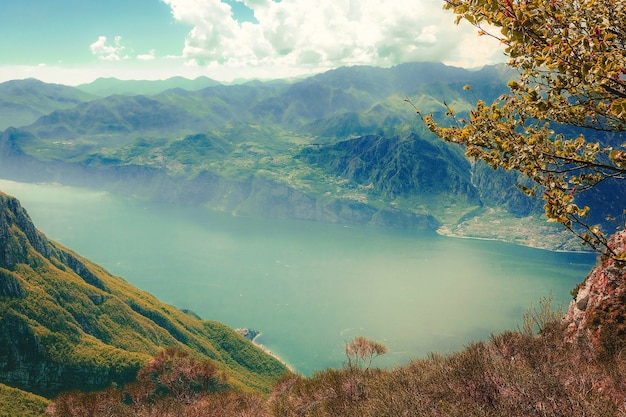 High Angle Shot of a Lake Surrounded by Green Mountains Covered in Fog Under the Cloudy Sky