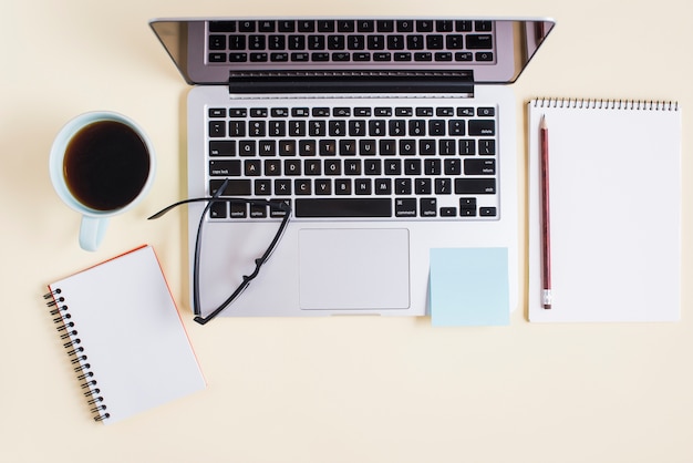 Laptop, Tea Cup, Spiral Notepad, Eyeglasses on Beige Backdrop – Free Stock Photo Download