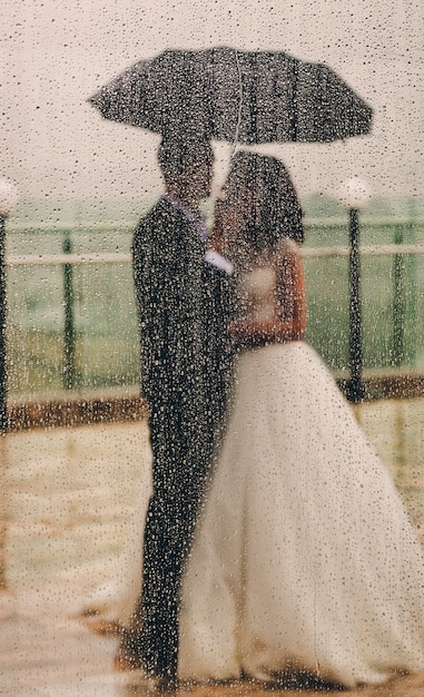 Wedding Couple Standing Under Umbrella Seen from Behind the Window