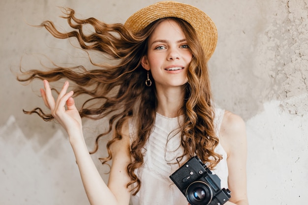 Young Pretty Smiling Happy Woman in White Blouse Sitting Against Wall in Straw Hat