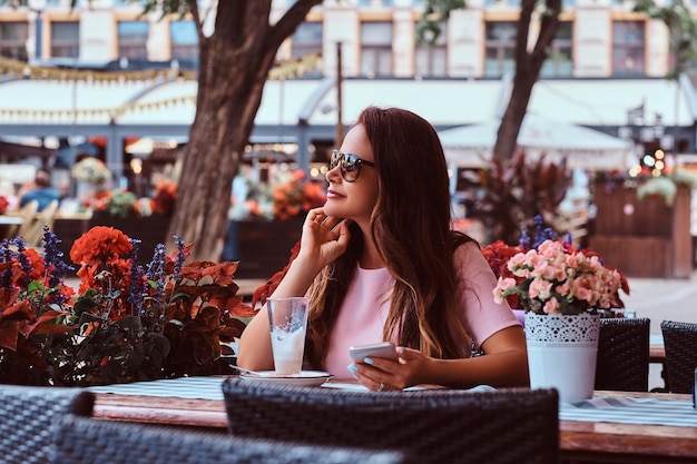 Portrait of a Middle Age Businesswoman with Long Brown Hair in Sunglasses Holding a Smartphone at an Outdoor Cafe