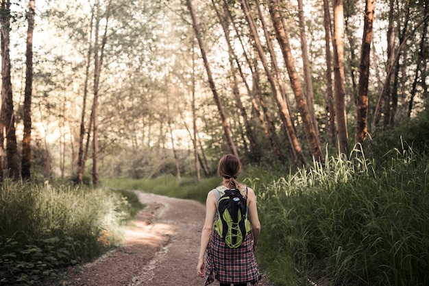 Rear view of woman walking on the dirt road in the forest