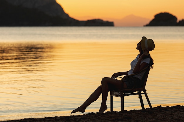 Young woman sitting on seat on sunset on the shore of a lake