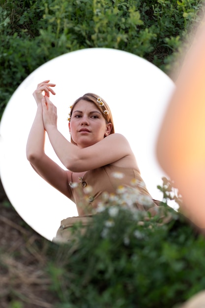 Young woman posing outdoors in a field using a round mirror