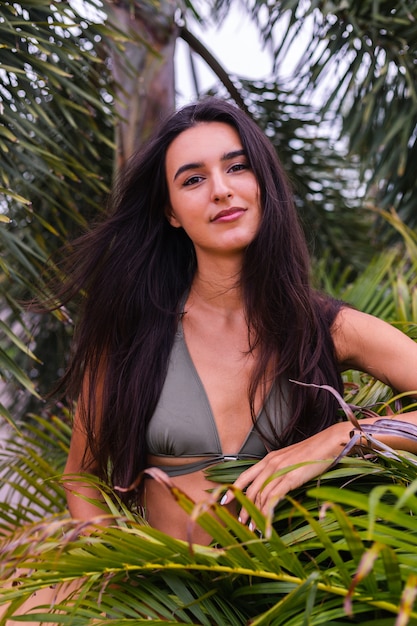 Portrait of fit tanned slim woman in green tiny bikini with tropical leaves