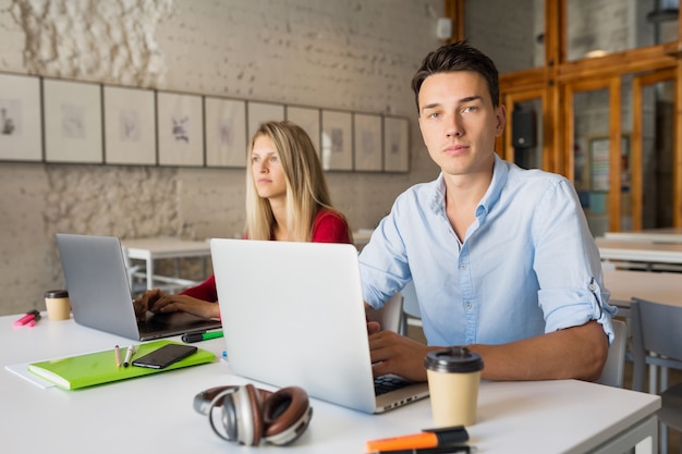 Young man and woman working on laptop in open space co-working office room