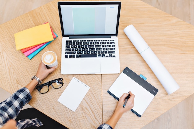 Hands of young woman working with laptop and holding a cup of coffee