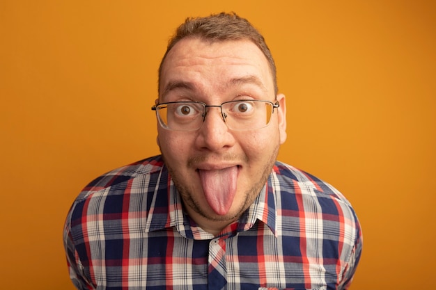 Funny Man in Glasses and Checked Shirt Sticking Out Tongue Standing Over Orange Wall