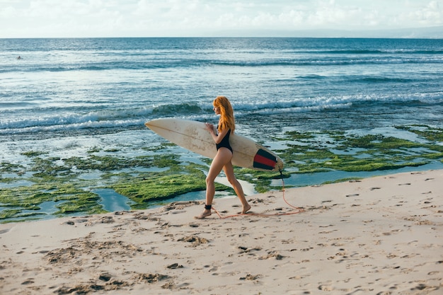 Young beautiful girl posing on the beach with a surfboard, woman surfer, ocean waves