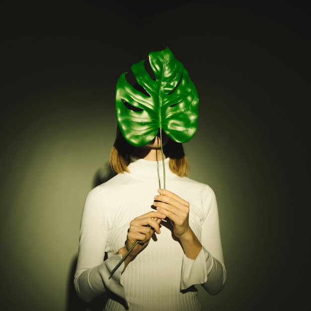 Woman covering face with green leaf