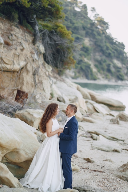 Long-Haired Bride in White Dress with Husband on Beach near Big Stones