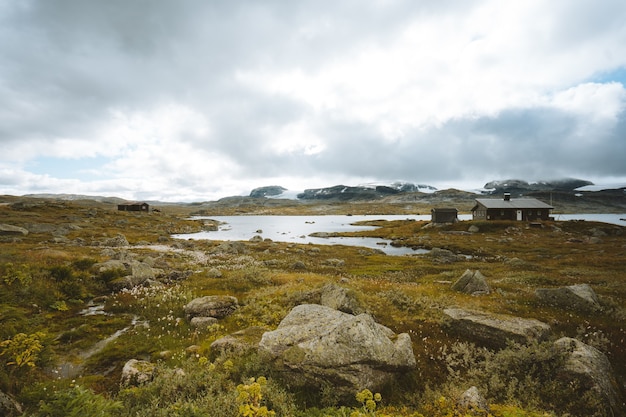 Landscape of a field surrounded by greenery and cabins under a cloudy sky in Finse, Norway – Free Stock Photo Download