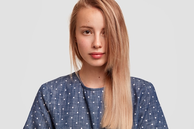 Cute Young Female with Long Hair in Polka Dot Blouse Poses Against White Wall