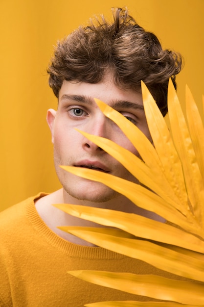 Young handsome man posing behind palm leaf in a yellow scene