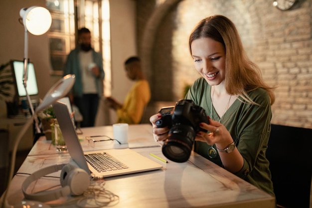 Happy female photographer checking images on digital camera while working at night in a studio