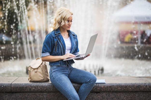 Busy Blonde girl woman student Working on Laptop Computer Near Fountain in the City