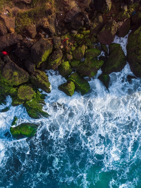 Vertical Aerial Shot of Wavy Blue Sea Against Rocks