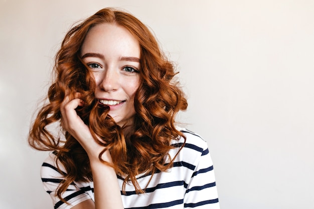 Blue-eyed ginger girl posing with happy smile. Indoor shot of amazing red-haired lady isolated