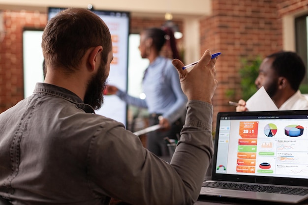 Businessman analyzing company graph on laptop computer working at management presentation during business meeting in startup office. Diverse businesspeople discussing collaboration project