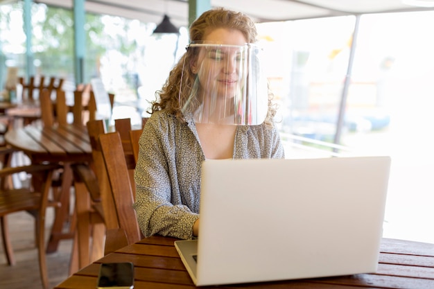 Woman wearing face protection while working on laptop – Free Stock Photo Download