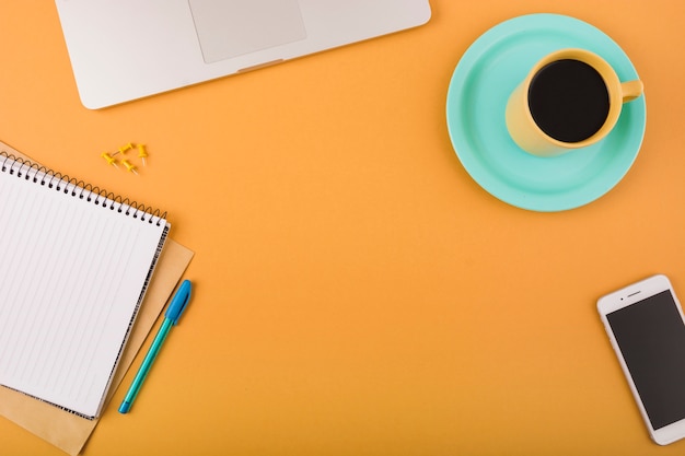 Black coffee; smartphone; laptop and notepad on orange backdrop