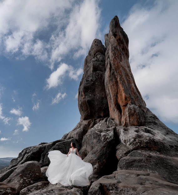 Beautiful Bride Standing on Rock Near High Cliff on Clear Day with Blue Sky