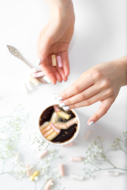 Coffee with marshmallows and women’s hands from the top view