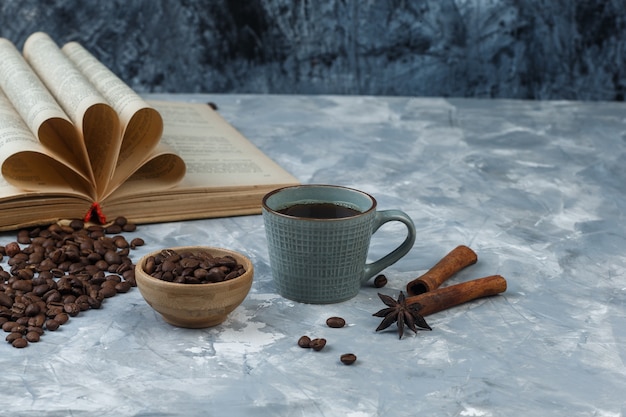 Coffee Beans in Wooden Bowl with Book, Cinnamon, Cup of Coffee High Angle View on Light and Dark Blue Marble Background