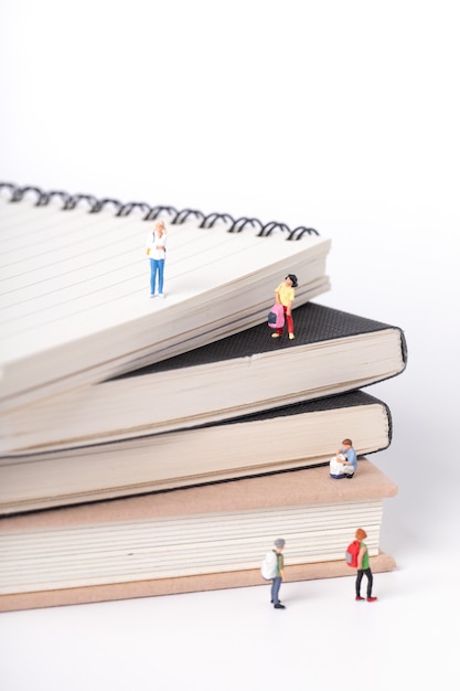 Vertical shot of little figurines of students standing on and around textbooks