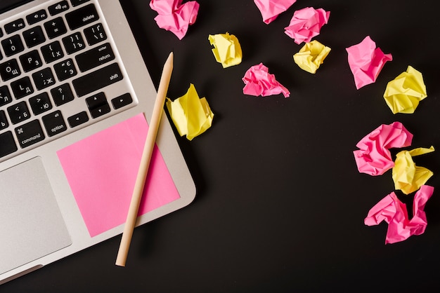 Ball of crumpled papers with adhesive note and pencil on laptop against black background