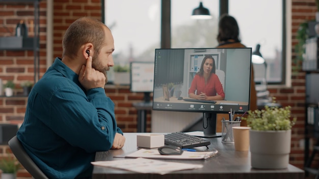 Employee talking to manager using video call and earpods on computer at desk. Business man attending meeting with colleague to discuss marketing strategy on remote online video conference.