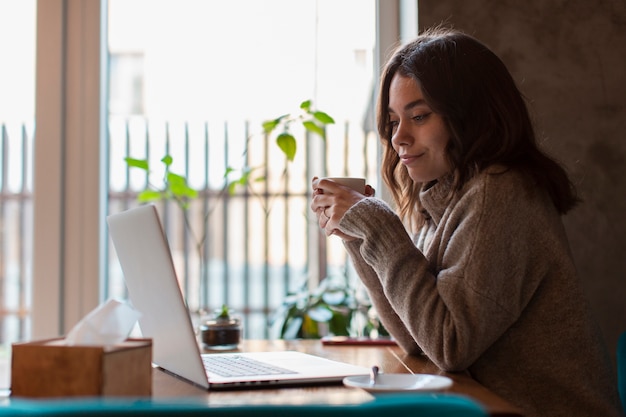 Woman Holding Cup and Looking at Laptop