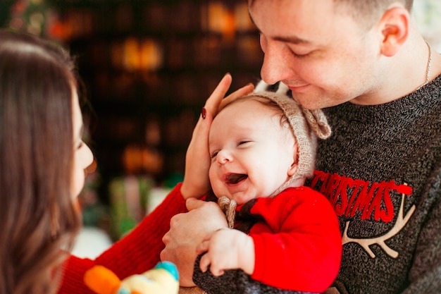 Parents Joyfully Play with Their Little Daughter in a Deer Hat by a Christmas Tree – Free Download