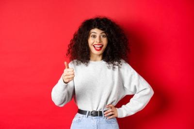 Happy Young Woman with Curly Hair Giving Thumbs Up on Red Background – Free Stock Photo, Download for Free