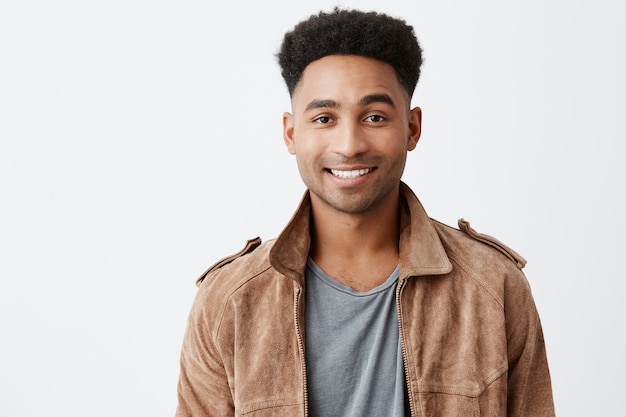 Young Dark-Skinned Guy Smiling with Afro Hairstyle in Grey T-Shirt and Brown Jacket – Free Stock Photo Download