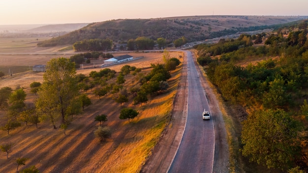 Country Road and Moving Car at Sunrise with Lush Fields and Tree-Covered Hills – Free Stock Photo Download