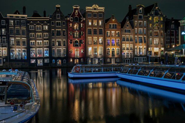 Traditional Houses and Cruise Boats at the Damrak in Amsterdam, Netherlands at Night – Free Download