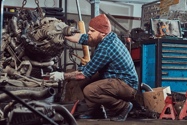 Brutal Tattooed Bearded Mechanic Working on Car Engine in Garage – Free Download