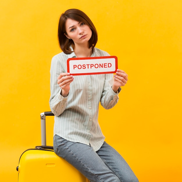 Woman Holding a Postponed Sign While Standing on Her Luggage – Free Download