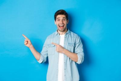 Handsome Young Man with Beard Pointing Left and Smiling Against Blue Background – Free Stock Photo for Download