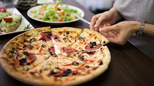 Close-up of a Woman’s Hand Taking a Slice of Pepperoni Pizza – Free Download