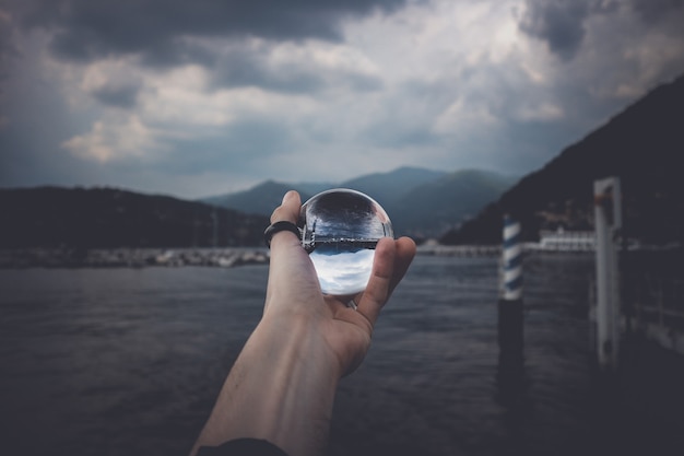 A Person Holding a Crystal Ball Reflecting Majestic Mountains and Beautiful Clouds – Free Download