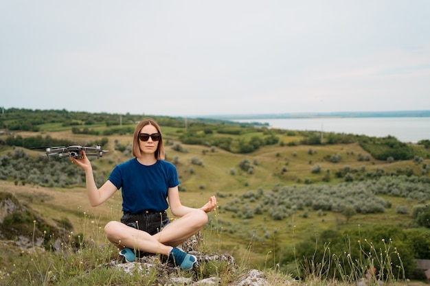 A Caucasian Woman Holding a Drone on a Green Rocky Hill with Sky – Free Download