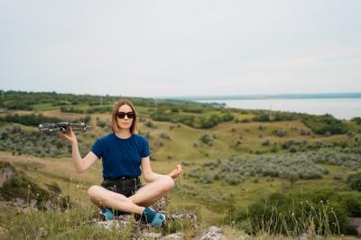 A Caucasian Woman Holding a Drone on a Green Rocky Hill with Sky – Free Download