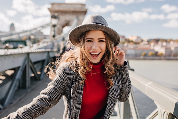 Winsome Curly Girl in Elegant Gray Hat Posing on Bridge on a Sunny Day – Free Download