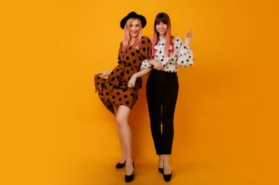 Two Elegant Women in Stylish Dresses Against a Yellow Wall – Free Download