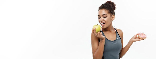 Healthy Lifestyle Choices: Sporty African American Woman Deciding Between Donut and Green Apple – Free Download